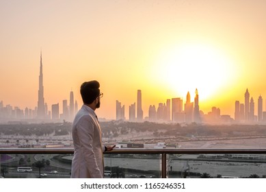 Guy in white suit looking at glowing sunset over the skyline of Dubai. Luxury travel inspiration. 