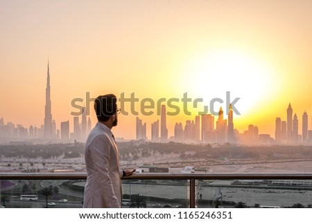 Guy in white suit looking at glowing sunset over the skyline of Dubai. Luxury travel inspiration. 
