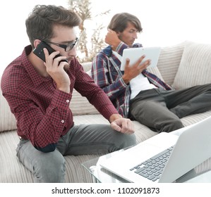 Mann, der auf Laptop arbeitet und auf Smartphone sitzt