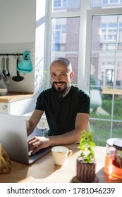The guy works from home. He sits in the kitchen at the table and uses a laptop computer and drink hot tea. He is smiling, his business is going well. - Shutterstock ID 1781046239