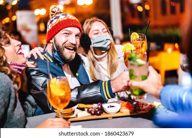 Guys And Girls Toasting Fancy Drink At Night Cocktail Bar Wearing Face Mask - New Normal Lifestyle Concept About Drunk Friends Having Fun Together Outside - Vivid Filter Focused On Man With Winter Hat