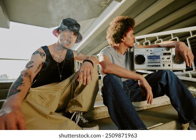 Guys partying together and sitting on stairs, young man smoking while curly haired one holding tape recorder - Powered by Shutterstock