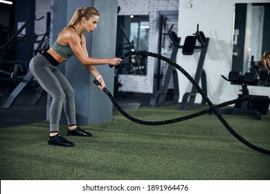 Gym attendant bending ahead and performing an exercise with battling ropes going up and down