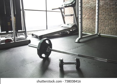 Gym Background With Barbell Dumbbell On The Empty Floor.Fitness Equipment For Weight Training Or CrossFit.