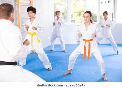 In gym, certified master coach conducts karate kata lesson with children boys girls team students group and shows sequence of actions when conducting close fight - Powered by Shutterstock