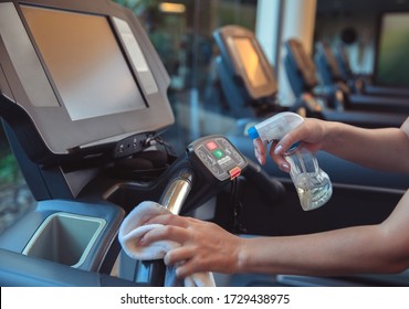 Gym cleaning and disinfection. Infection prevention and control of epidemic. Staff using wipe and alcohol sanitizer spray to clean treadmill in gym.