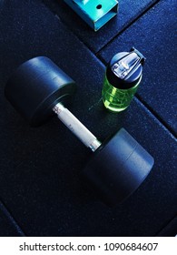 The Gym. A Dumbell & Bottle Together. A Blue Hue Surrounds The Image.