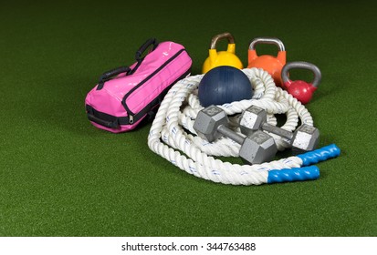 Gym Equipment For Bootcamp Classes.  Kettle Bells, Rope, Dumbbells, Medicine Balls, And Pink Sand Bag On Green Turf