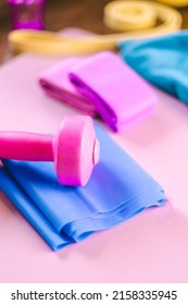 Gym Equipments On A Pink Yoga Mat. Blue Rubber Band, Blue And Pink Resistance Band And Pink Dumbell