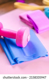 Gym Equipments On A Pink Yoga Mat. Blue Rubber Band, Blue And Pink Resistance Band And Pink Dumbell