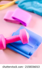 Gym Equipments On A Pink Yoga Mat. Blue Rubber Band, Blue And Pink Resistance Band And Pink Dumbell