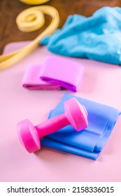 Gym Equipments On A Pink Yoga Mat. Blue Rubber Band, Blue And Pink Resistance Band And Pink Dumbell