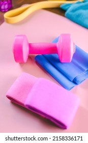 Gym Equipments On A Pink Yoga Mat. Blue Rubber Band, Blue And Pink Resistance Band And Pink Dumbell