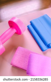 Gym Equipments On A Pink Yoga Mat. Blue Rubber Band, Blue And Pink Resistance Band And Pink Dumbell