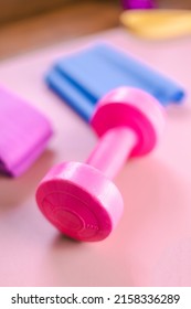 Gym Equipments On A Pink Yoga Mat. Blue Rubber Band, Blue And Pink Resistance Band And Pink Dumbell