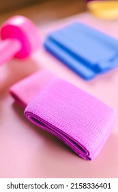 Gym Equipments On A Pink Yoga Mat. Blue Rubber Band, Blue And Pink Resistance Band And Pink Dumbell