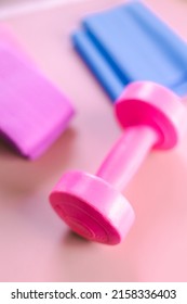 Gym Equipments On A Pink Yoga Mat. Blue Rubber Band, Blue And Pink Resistance Band And Pink Dumbell