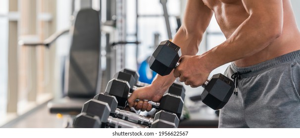 gym and fitness background banner of close up dumbbell with hand of athletic bodybuilder man lifting from dumbbell rack in gym and fitness club