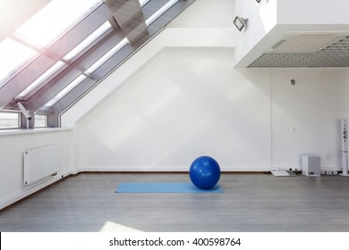 Gym For Fitness Exercises. Fitball And Mat  Lie On The Floor. The Room Is Flooded With Daylight Sunlight From The Window, The Glare On The White Wall. Audio System With Speakers In The Background.