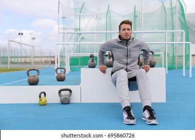 Gym fitness man training arms muscles doing triceps dips at outdoor training centre at stadium. Sport athlete in sweatpants sportswear outside.