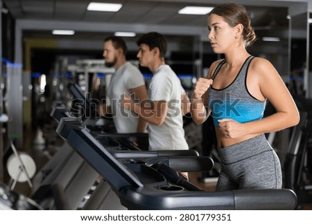 In gym, girl does exercises using treadmill. Young group of athletes trains in gym. Physical education and sports, active healthy lifestyle.