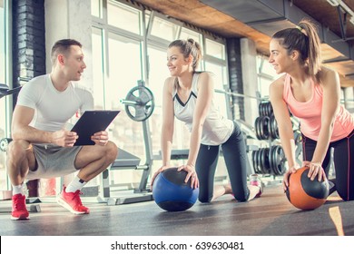 Gym instructor assisting two sporty women with pilates balls in fitness center. - Powered by Shutterstock