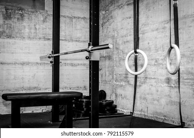 Gym interior closeup of benchpress  bench gymnastics rings and barbell plate weights on the floor in the corner hard core black and white dark image