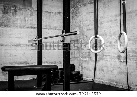 Gym interior closeup of benchpress  bench gymnastics rings and barbell plate weights on the floor in the corner hard core black and white dark image