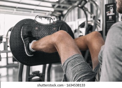 Gym Leg Press machine fit man training legs workout on fitness machine doing heavy weights pushing with hamstring and quads muscles.
