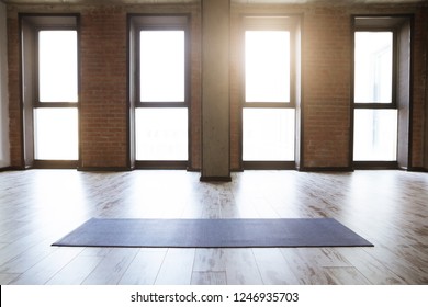 Gym Loft Interior With Blue Yoga Mat, Big Windows And Sunlight, No People. Copy Space