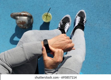 Gym man touching smartwatch screen during workout strength training. Top view from above: kettlebell weights, green smoothie, body and legs. POV of athlete sitting resting. Healthy fitness lifestyle.