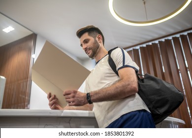 Gym Services. Male Customer Standing At Recepion Desk, Reading Carefully Price List