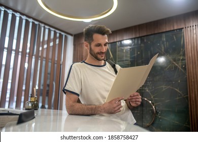 Gym Services. Male Customer Standing At Recepion Desk, Studying Price List