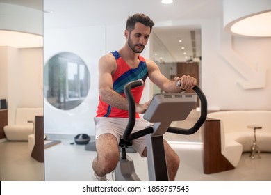 Gym. Sporty man in bright tshirt exercising on a gym machine