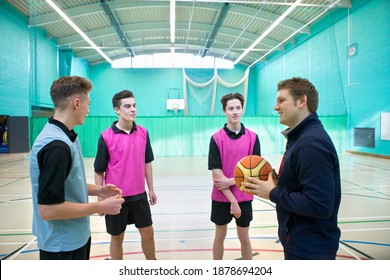 Gym Teacher With A Basketball Speaking To High School Students In A Gym.