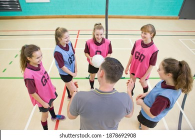 Gym Teacher Talking To A Group Of High School Girls About Netball In A Gym Class.