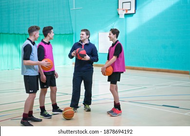 Gym Teacher Teaching Basketball To A Group Of High School Students In A Gym.