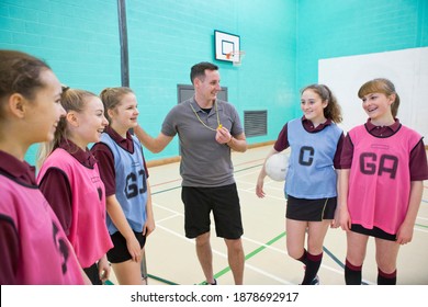 Gym Teacher With A Whistle Talking To High School Students With A Netball In A Gym.