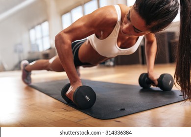 Gym woman doing push-up exercise with dumbbell. Strong female doing crossfit workout. - Powered by Shutterstock