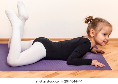 Gymnast child doing flexibility exercise on a purple mat. Home training of a little ballerina