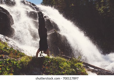 The gymnast performs a dangerous trick on the edge of a cliff on the background of beautiful waterfall. Extreme camping. - Powered by Shutterstock