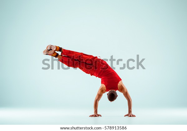 The gymnastic acrobatic caucasian man\
posing in balance posture on gray studio\
background
