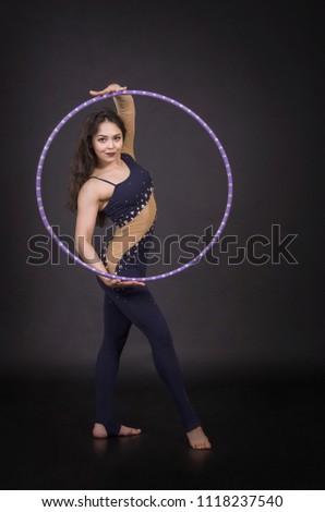 Gymnastic exercises with hula-Hoop girl performs circus performer in an artistic costume. Studio shooting on a dark background.