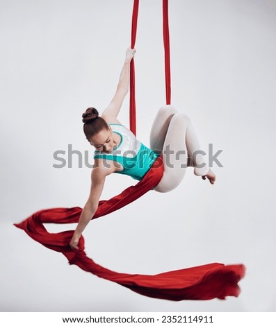 Gymnastics, aerial acrobat and sports with a woman in air for performance and balance. Young athlete person or gymnast hanging on red silk fabric and white background with space, art and creativity