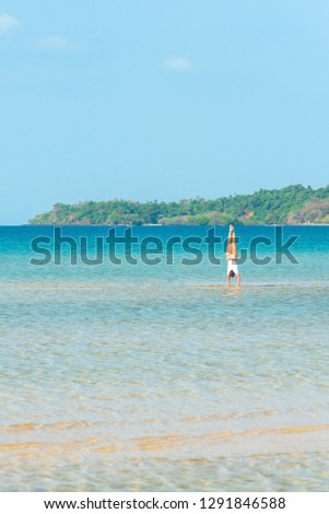 Gymnastics by the sea, a portrait of attractive young girl gymnast training exercise in the blue sea in sunny, rear view of perfect fit shape body, tropical island backdrop.