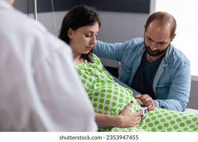 Gynecologist checking pregnant woman symptoms before medical surgery, discussing childbirth process with future parents in hospital ward. Patient with pregnancy lying in bed in maternity clinic - Powered by Shutterstock