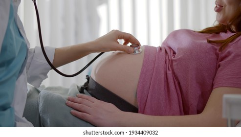 Gynecologist doctor hand checking pregnant young woman with stethoscope. Obstetrician checking up pregnant woman belly lying in bed at hospital