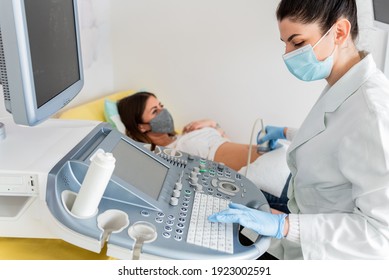 Gynecologist doctor wearing protection face mask does ultrasound, sonogram procedure to a pregnant woman. Pandemic time and health care concept.