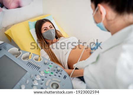 Gynecologist doctor wearing protection face mask does ultrasound, sonogram procedure to a pregnant woman. Pandemic time and health care concept.