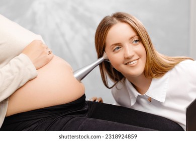 A gynecologist leans a stethoscope to a pregnant woman's belly and listens to the baby's heartbeat. - Shutterstock ID 2318924859